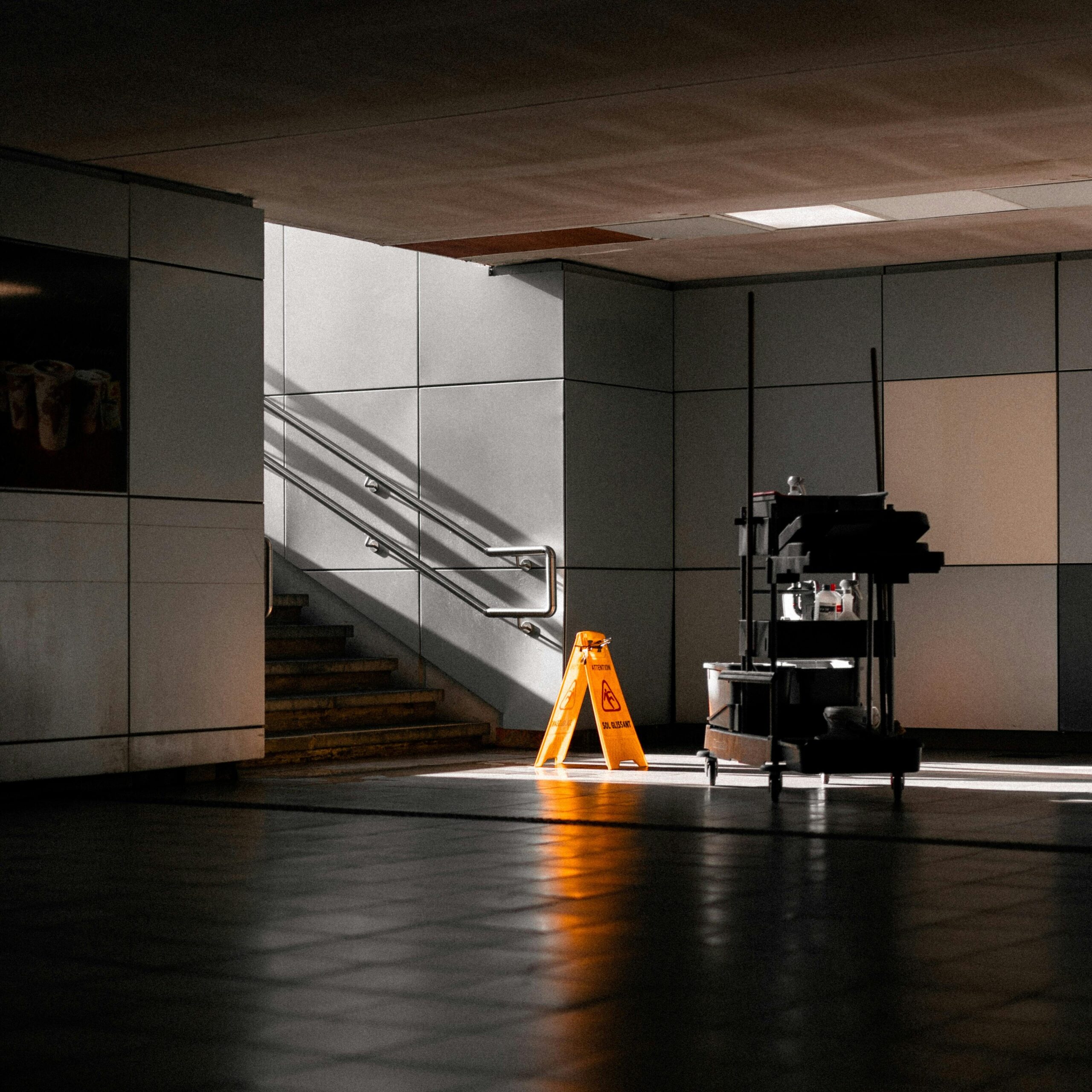 A well-lit underground corridor featuring stairs, cleaning supplies, and warning signs.